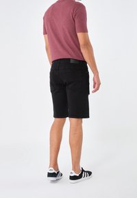 Pantalones cortos de mezclilla negra con un corte recto, que cuentan con bolsillos traseros y una cintura texturizada. Se llevan con una camisa color burdeos y zapatillas negras.