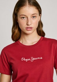 Raudona medvilninė marškinė su apvalia iškirpte, trumpomis rankovėmis ir balta siuvinėta "Pepe Jeans London" logo priekyje. Lygaus paviršiaus.