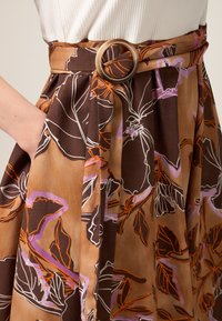 Gonna floreale in tessuto marrone con dettagli arancioni e viola, dotata di una vita ampia e di un particolare cinturino circolare, con tasche laterali.