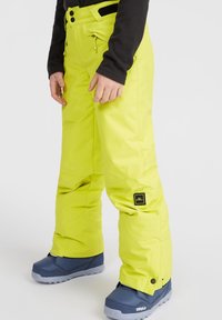 Pantaloni da neve gialli brillanti con un esterno impermeabile, vita regolabile e tasche con zip. Abbinati a stivali invernali blu navy.