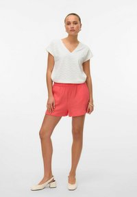 Witte V-hals, kort mouw blouse met zigzagtextuur, gecombineerd met koraal, geplooide shorts. Draag het met crèmekleurige schoenen met blokhak.