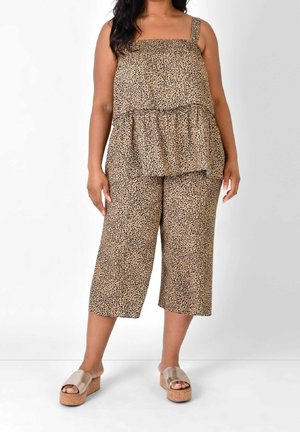 Mujer con top sin mangas con estampado de leopardo y pantalones anchos cortos con sandalias de plataforma beige, de pie frente a un fondo blanco.