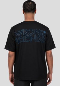 Černé bavlněné tričko s krátkým rukávem, které na zádech zdobí velký modrý nápis "WRONG FRIENDS". Jednoduchý, standardní fit design.