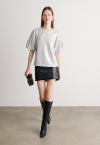 Hõbedane sädelev lühikeste varrukatega topp, must nahkne mini seelik, põlvekõrgused mustad saapad, must käekott käes. Lihtne, modernne siluett.