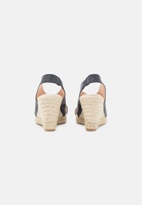 Sandálias de cunha em pele azul marinho com salto envolto em juta, costas abertas e tira no tornozelo. A sola texturizada proporciona aderência e conforto.