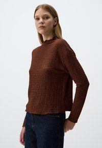 Haut long à manches, texturé et marron, avec un col froncé et une coupe légèrement cropped, assorti à un jean en denim noir.