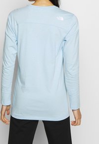 Vaaleansininen pitkähihainen paita, jossa pyöreä pääntie ja logo yläselässä. Pehmeä kangas, väljähkö istuvuus ja vyötärön pituinen helma.