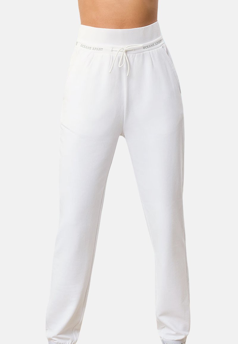 Białe dresy wykonane z miękkiego materiału, posiadające elastyczny pas w talii ze sznurkiem oraz zwężane nogawki, zapewniające luźny fason.