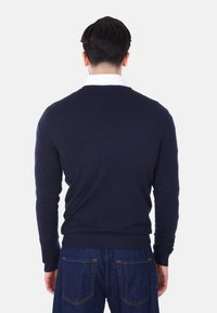 Maglione blu in maglia con maniche lunghe, polsini e orlo a coste, caratterizzato da una texture liscia e scollatura rotonda. Indossato sopra jeans blu.