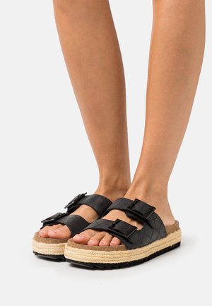 Sandales plateforme en cuir noir avec deux sangles réglables à boucle, semelle intermédiaire en jute tissé, semelle extérieure texturée et design ouvert à l'avant.