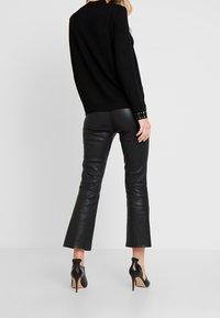 Schwarzer Strickpullover mit schlichter Rückseite, ausgestattet mit gesteppter Detail an den Handgelenken, kombiniert mit schwarzen, ausgestellten Lederhosen und schwarzen High Heels.