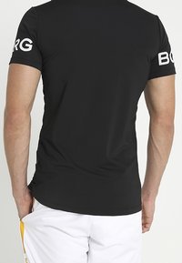 Camiseta atlética negra de manga corta, con el texto "BORG" en blanco en el hombro izquierdo. Textura suave, diseño ajustado.