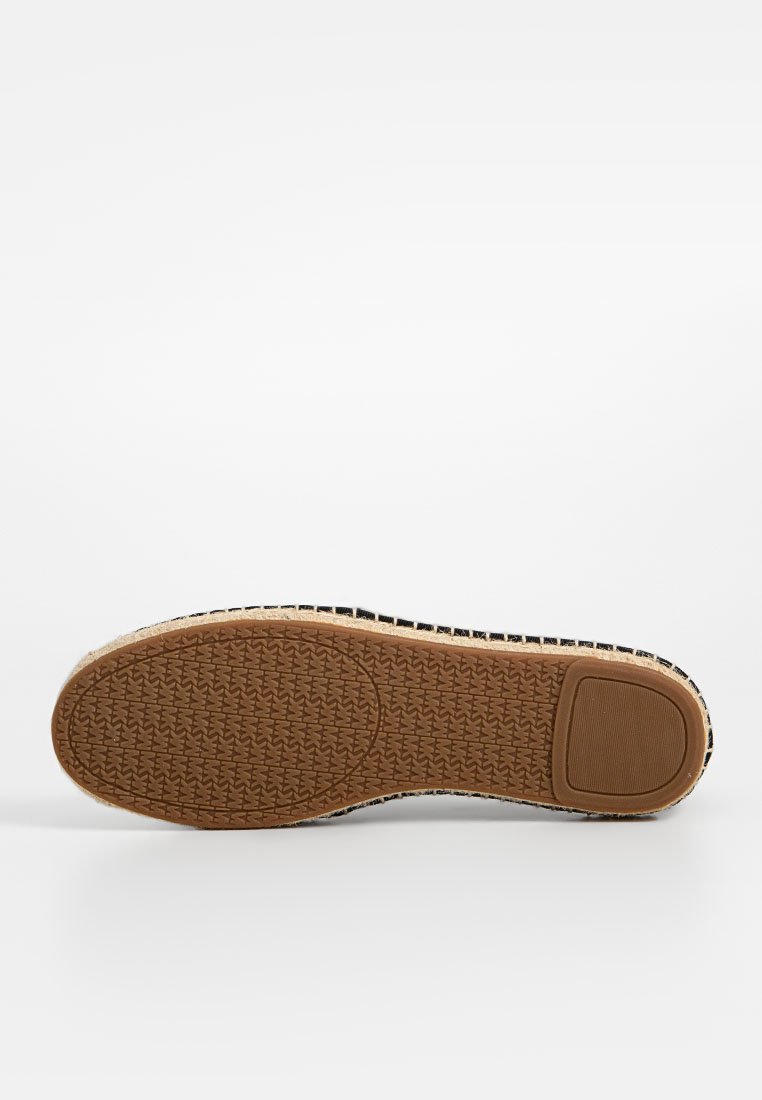 Suola in gomma con un design testurizzato e a motivi in marrone. I bordi mostrano un tessuto intrecciato con una combinazione di colori bianco e nero.