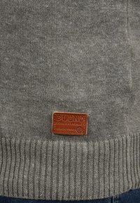 Pull en maille gris avec ourlet côtelé ; présente une étiquette en cuir marron rectangulaire embossée avec "BLEND GLOBAL JEANMAKER SINCE 1993."