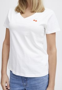 Weißes Baumwoll-T-Shirt mit V-Ausschnitt, ausgestattet mit einem kleinen, in Orange gestickten Kirschmotiv auf der linken Brust. Leichter Stoff.