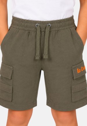 Enfant portant un short cargo vert olive avec plusieurs poches latérales et une taille à cordon, les mains dans les poches, chemise blanche partiellement visible.