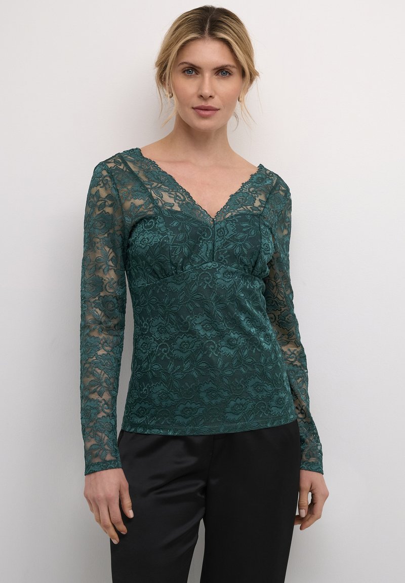 Top in pizzo teal con maniche lunghe, scollatura a V, motivo floreale e design aderente, abbinato a pantaloni in satin neri. Dettaglio testurizzato in tutto il capo.