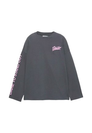 Hosszú ujjú, sötétszürke pamut póló. Mellrészen rózsaszín logó, a bal ujjon pedig az "Merj kitűnni" felirat található.