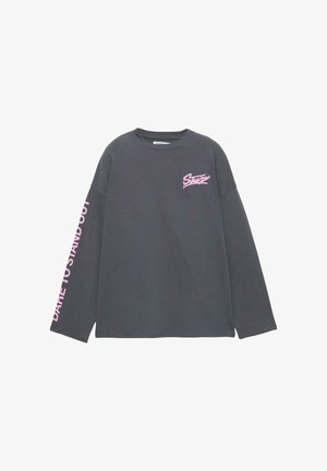 Hosszú ujjú, sötétszürke pamut póló. Mellrészen rózsaszín logó, a bal ujjon pedig az "Merj kitűnni" felirat található.