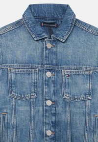 Veste en denim bleu moyen, dotée d'un col classique, de boutons-pression en argent, de deux poches poitrine et d'une étiquette logo de la marque au niveau du col.