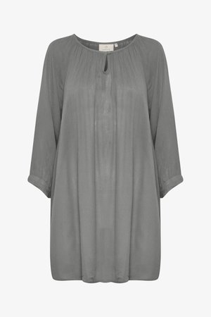 Blouse ample à manches longues en tissu gris doux. Présente un détail de décolleté en trou de clé, des plis texturés et des poignets retroussés. Matière lisse et légère.