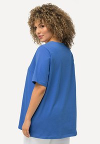 Modré tričko s krátkým rukávem, volného střihu, kulatým výstřihem a hladkým povrchem, zobrazené zezadu. Minimální švy a čistá silueta.