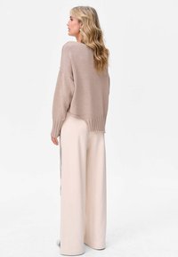 Beżowy sweter dzianinowy z prążkowanym dołem, o nieco oversize'owym kroju. Połączony z beżowymi szerokimi spodniami i subtelnymi bocznymi paskami.