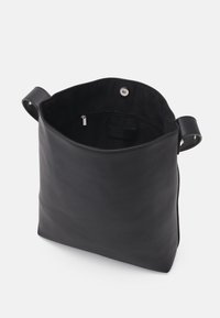 Sac fourre-tout en cuir noir avec une texture lisse, ouvert en haut, et deux poignées ; l'intérieur comporte une poche zippée et une doublure en tissu.