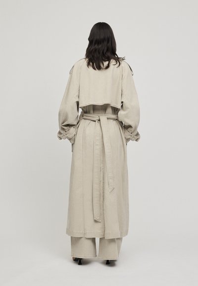 Cappotto beige con corpino corto, maniche lunghe e vita cintata. Presenta pantaloni a gamba larga nello stesso tessuto e colore.