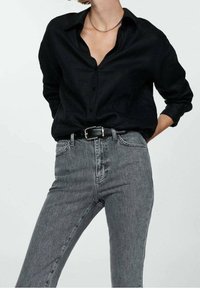 Czarna koszula z guzikami, wykonana z teksturowanej tkaniny, o luźnym kroju. Połączona z szarymi dżinsami o klasycznym kroju i subtelnych detalach w szyciu.