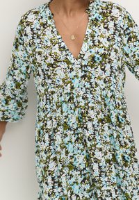 Robe florale avec un décolleté en V, des manches cloches trois-quarts et une taille froncée. Les couleurs comprennent des motifs floraux bleus, verts et noirs.
