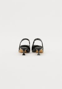 Črne usnjene slingback visoke pete s kvadratnim nosom in nizko, nagnjeno peto. Gladka tekstura in minimalističen dizajn, ki vključuje trak za gleženj.
