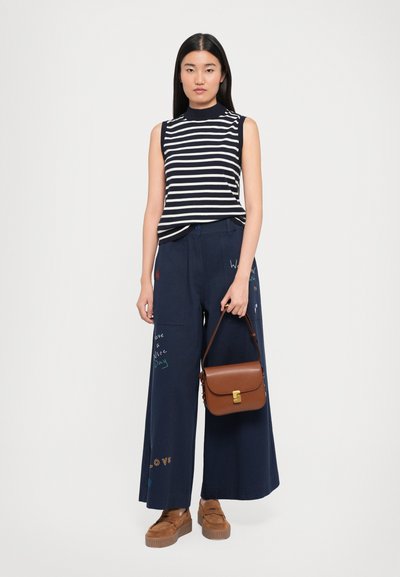 Striped sleeveless top, navy wide-leg pants with colorful text, brown handbag with gold hardware, and brown platform shoes.