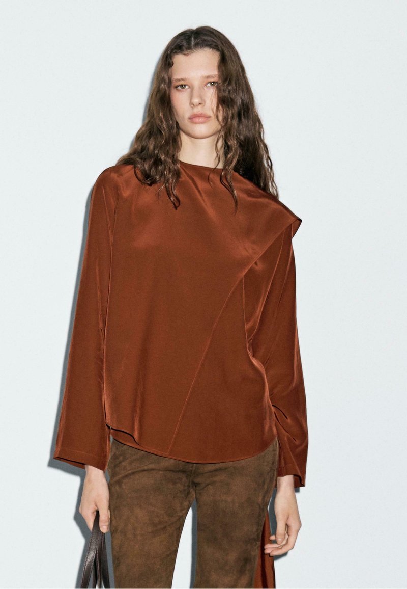 Brun satin langærmet bluse med asymmetrisk design. Blød tekstur, afslappet pasform og minimalistisk stil. Sammen med brun ruskindsbukser.