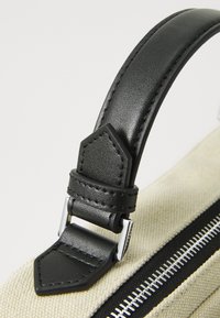 Canvas bag with a black leather strap. The strap features silver hardware and a stitched detail at the attachment point.