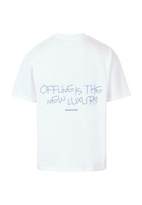 Bílý bavlněný tričko s modrým nápisem na zádech, který zní "OFFLINE JE NOVÝ LUXUS" s "DALŠÍ BAVLNA" níže.