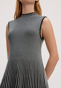 Schwarz-weißer gestreifter ärmelloser Kleid mit hohem Kragen, ausgestattet mit einem figurbetonten Oberteil und einem weit schwingenden Rock. Texturiertes Gewebe mit dezentem Glanz.
