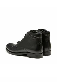 Bottes basses en cuir noir avec bout rond, lacets et finition lisse. Elles présentent un petit talon empilé et des détails de coutures discrètes sur les côtés.