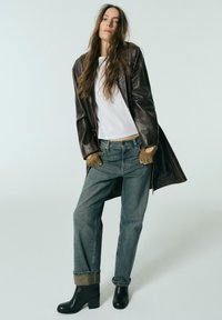 Brown leather coat, white short-sleeve shirt, faded blue jeans with rolled cuffs, and black heeled ankle boots. Textured soft materials.