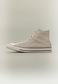 Μπεζ υφασμάτινο ψηλό αθλητικό παπούτσι με λευκή καουτσούκ σόλα και κάλυμμα στα δάχτυλα, λευκά κορδόνια και μεταλλικά ροδέλες, εμφανίζεται σε προφίλ σε ουδέτερο φόντο.