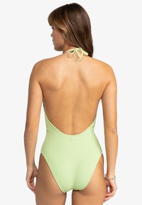 Maillot de bain une pièce vert à côtes avec un dos nu et un lien derrière le cou. Dispose d'une texture lisse et de minimalistes accents en matériel.