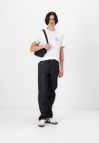 Hvid bomulds t-shirt med grøn tryk, mørkeblå denimjeans og en sort crossbody taske. Skoene er hvide med grå og sorte accenter.