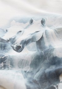 Tissu blanc présentant une impression aux tons bleus de deux têtes de cheval, avec une texture lisse et des dégradés subtils mettant en valeur le design.