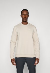 Sweatshirt bege com um decote redondo, mangas longas, punhos e bainha canelados, com um logótipo subtil no peito. Textura suave.