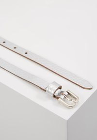 Ceinture en cuir blanc texturé avec une boucle et une garde en métal argenté. Elle possède cinq trous d'ajustement et des bords lisses.