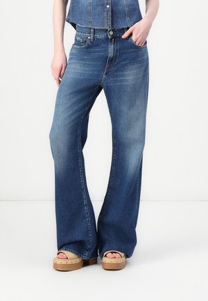 Vida byxa i blå denim med en blekt tvätt, utrustad med fem fickor och knappstängning. Kombineras med träplattformssandaler.