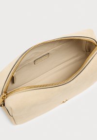 Μπεζ σουέντ θήκη με χρυστό φερμουάρ, με ομαλή υφή και απλό εσωτερικό. Περιλαμβάνει μια μικρή εσωτερική τσέπη και ταμπέλα με το λογότυπο.