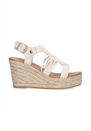 Sandalia cuña en crema, con diseño de tiras trenzadas, hebilla ajustable en el tobillo y suela de cuerda texturizada. Elevación: moderada.
