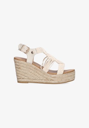 Sandalia cuña en crema, con diseño de tiras trenzadas, hebilla ajustable en el tobillo y suela de cuerda texturizada. Elevación: moderada.
