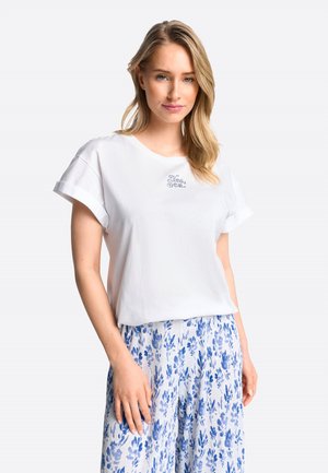 Witte katoenen t-shirt met opgerolde mouwen, voorzien van geborduurde tekst "Ja, Zee." Gecombineerd met lichtblauwe, met bloemenpatroon, wijde broek.